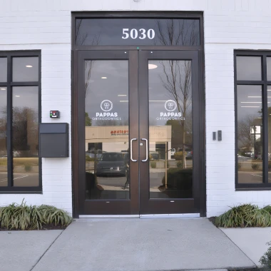 Entrance doors of Pappas Orthodontics featuring logo, street number, lantern lights, and landscaping.